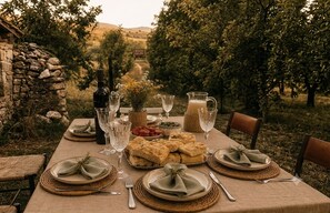 An outdoor dining table set with plates, glasses, and a bottle, surrounded by a stone wall and trees. - A rustic cabin nestled in the mountainous landscape of Majella National Park (Abruzzo)