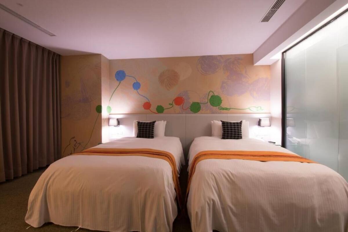 Ein Hotelzimmer mit zwei Betten, einem Wandgemälde und einem großen Fenster.