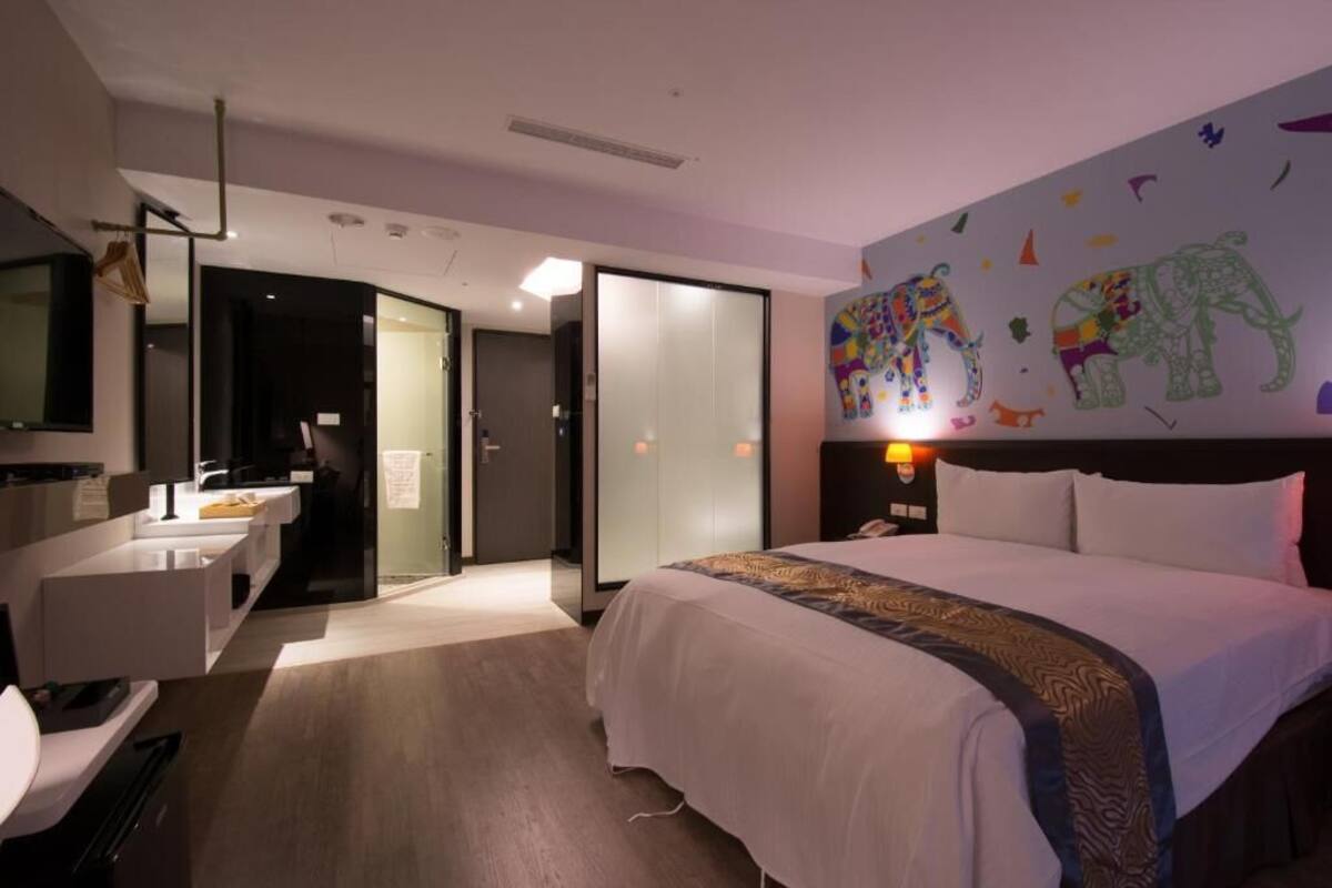 Ein Hotelzimmer mit Bett, Schreibtisch, Stuhl, Bad und einer Wand mit Elefantenmotiven.