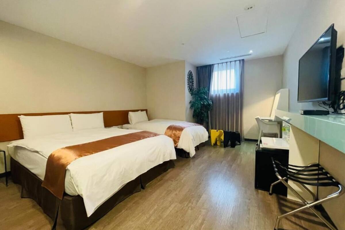 Ein Hotelzimmer mit zwei Betten, einem Schreibtisch, einem Stuhl, einem Fernseher und einer Pflanze.