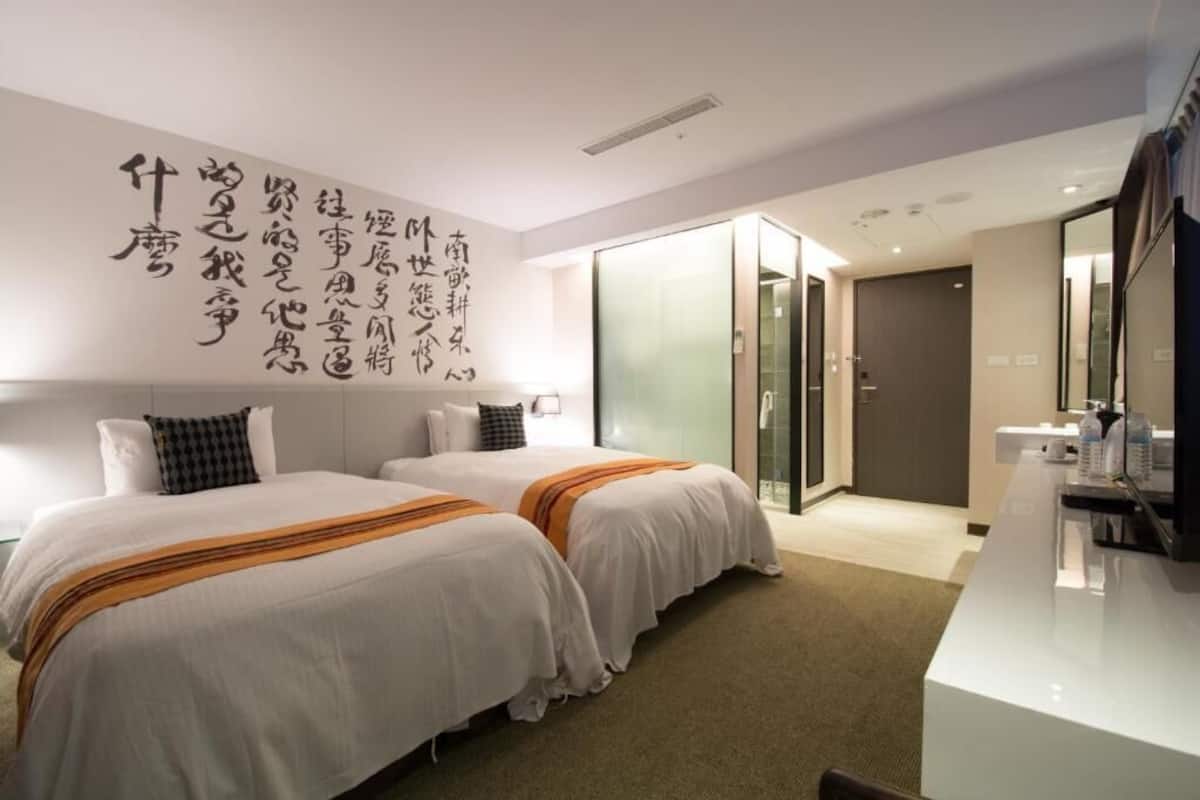 Ein Hotelzimmer mit zwei Betten, einem Schreibtisch und einem Spiegel.