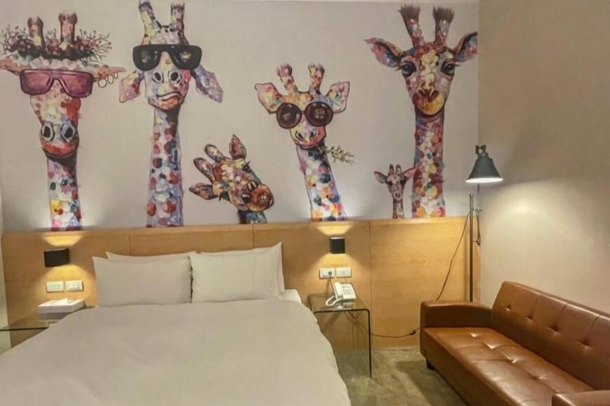 Ein Hotelzimmer mit Bett, einer braunen Ledersofa, einem Nachttisch mit Lampe und einer Wand mit Giraffenbildern.