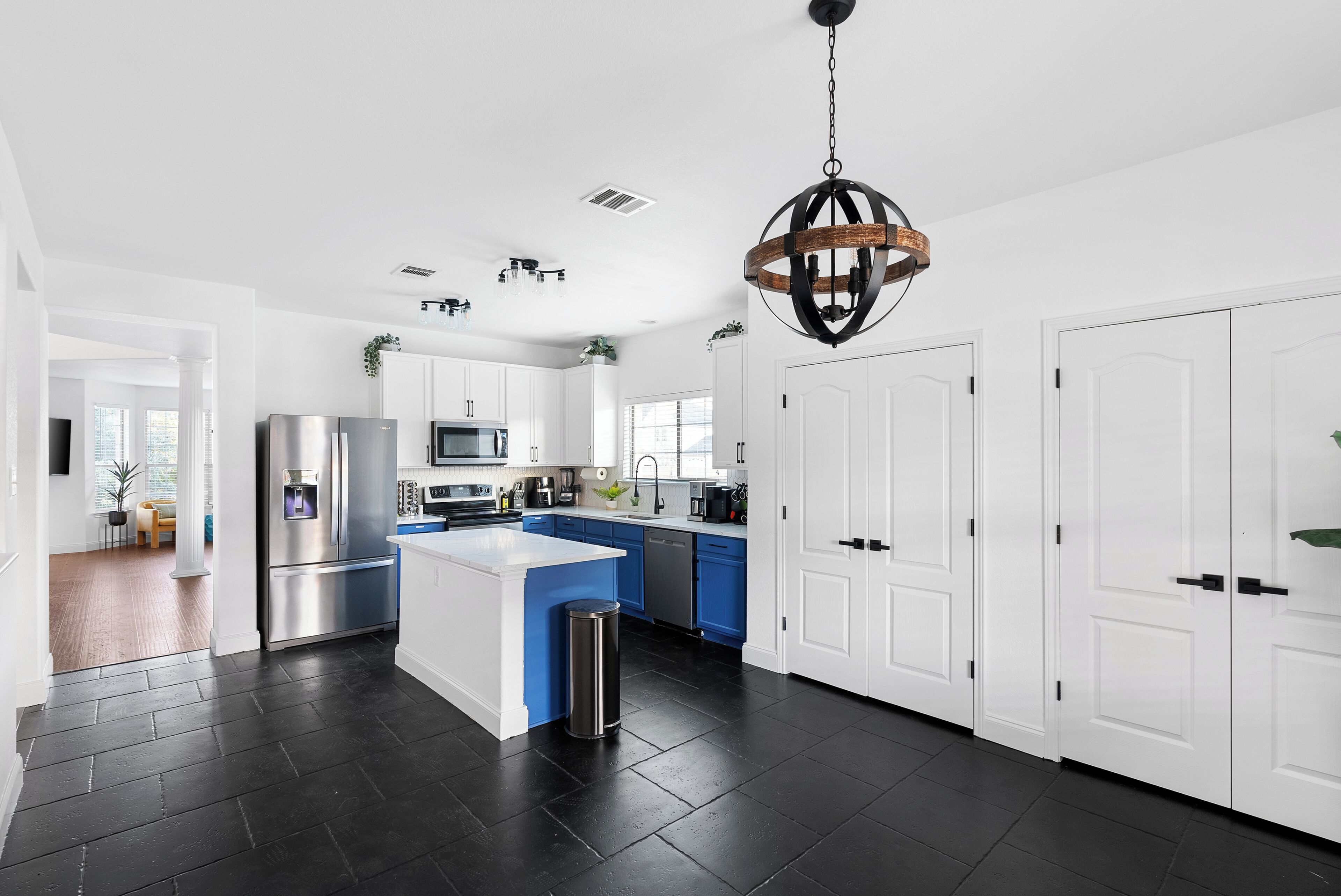 A modern kitchen with white cabinetry, a central island, stainless steel appliances, and a hanging light fixture.