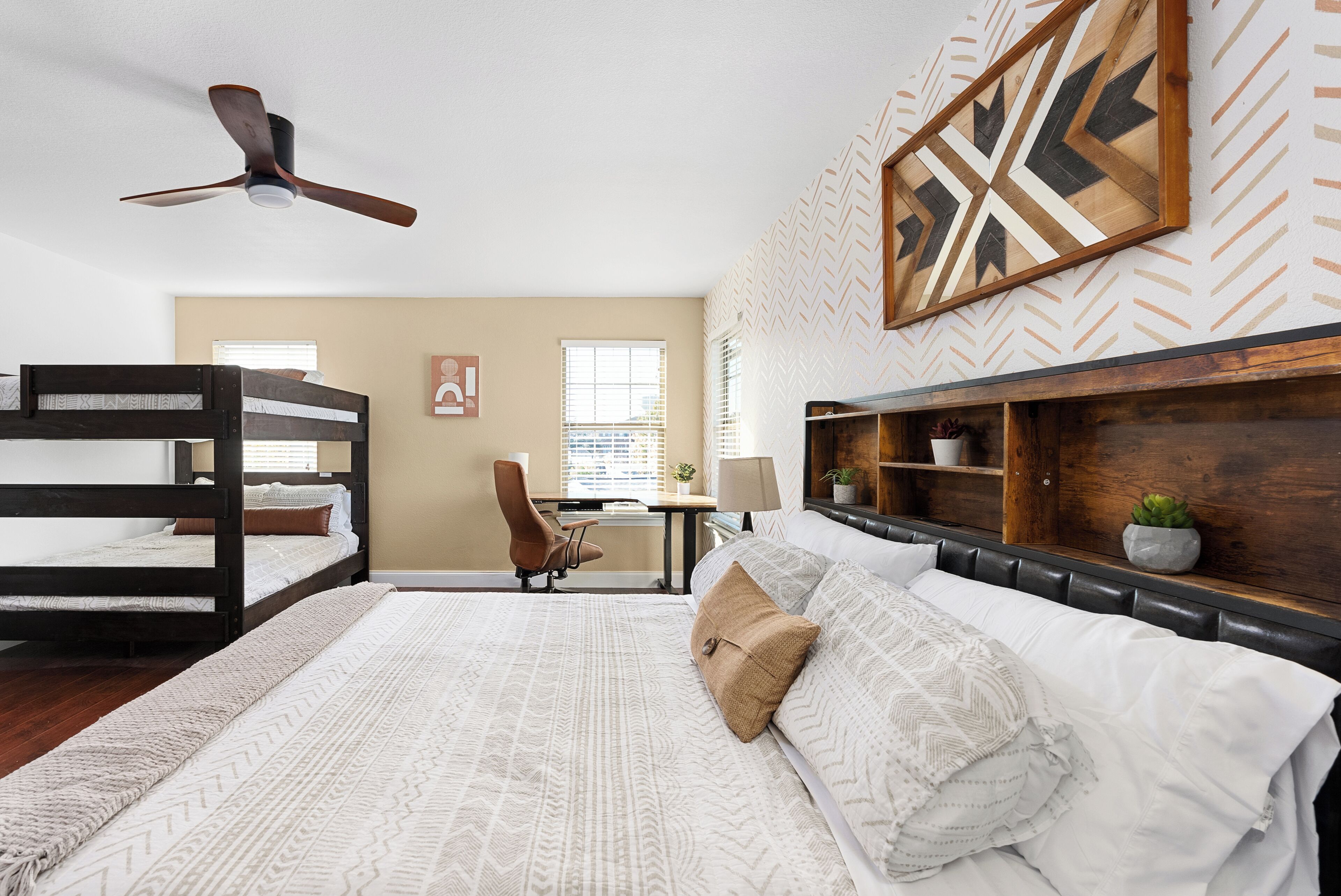 A bedroom with bunk beds, a desk, a chair, a ceiling fan, and a decorative wall piece.