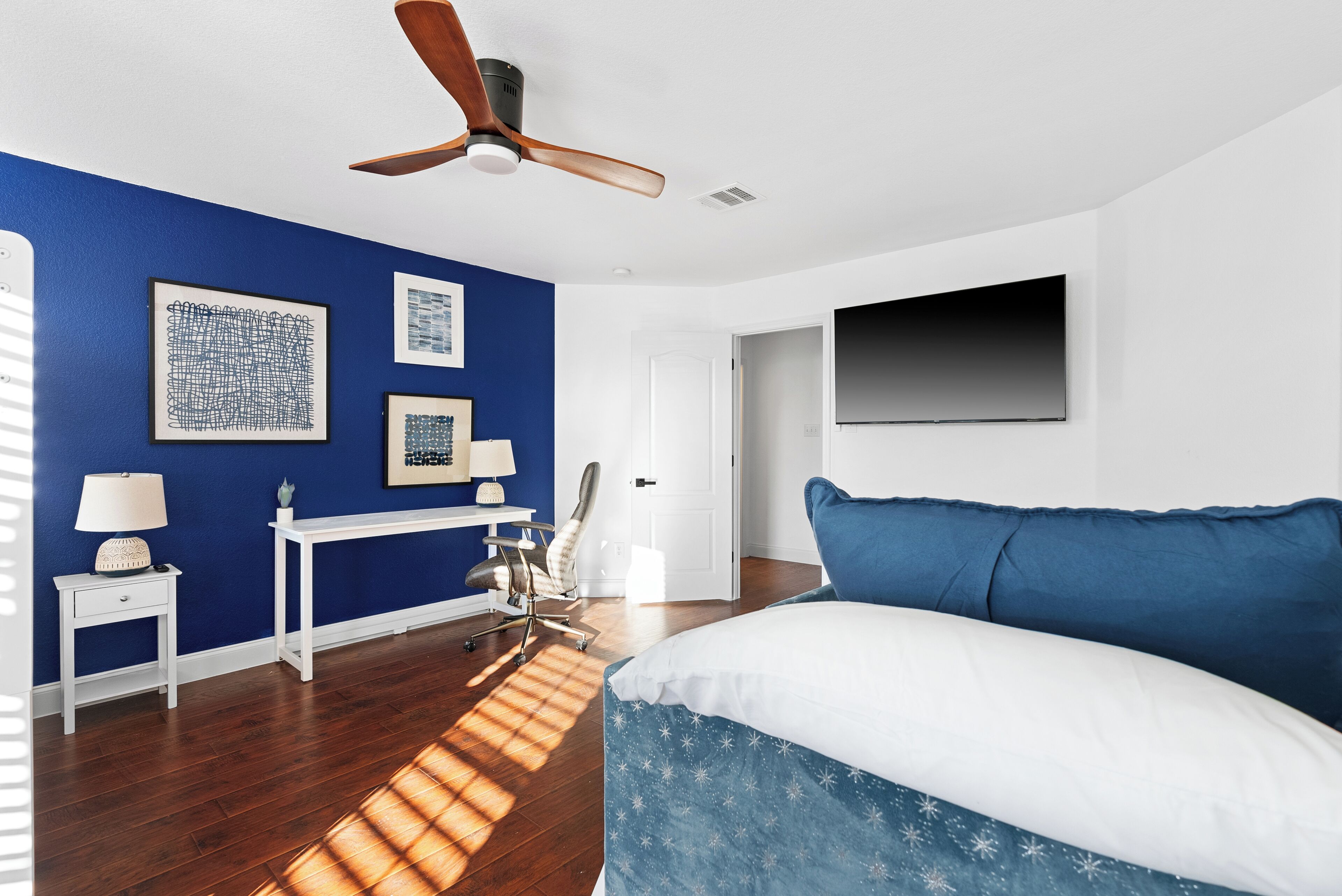 A bedroom with a bed, a desk, a chair, and a ceiling fan.