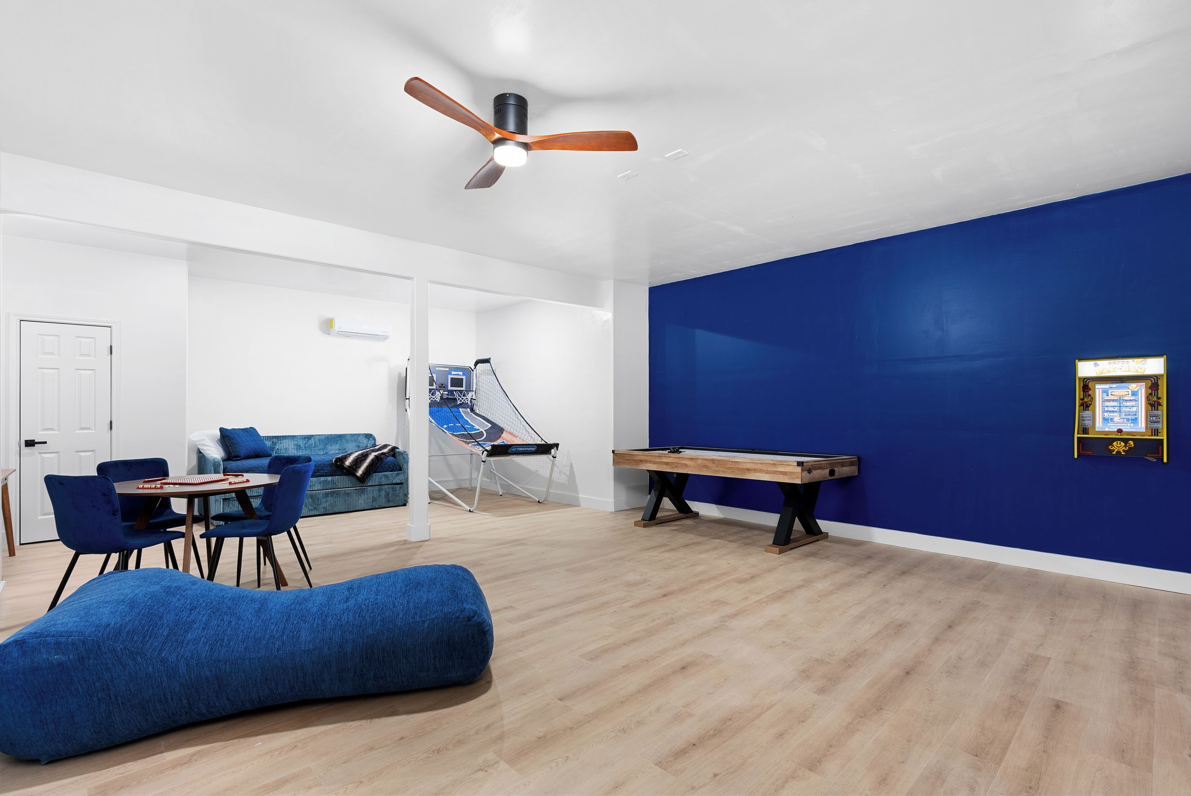 Une pièce avec un mur d’accent bleu, un ventilateur de plafond, une table de billard, un canapé bleu, une chaise bleue et une petite table avec des chaises.