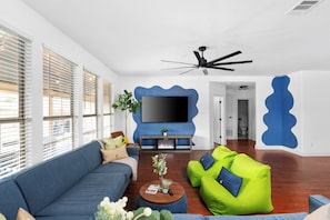 A modern living room with a blue accent wall, a flat-screen TV, a ceiling fan, and a fireplace. - Grand 6BR 3BA Pool Escape Round Rock (Round Rock)