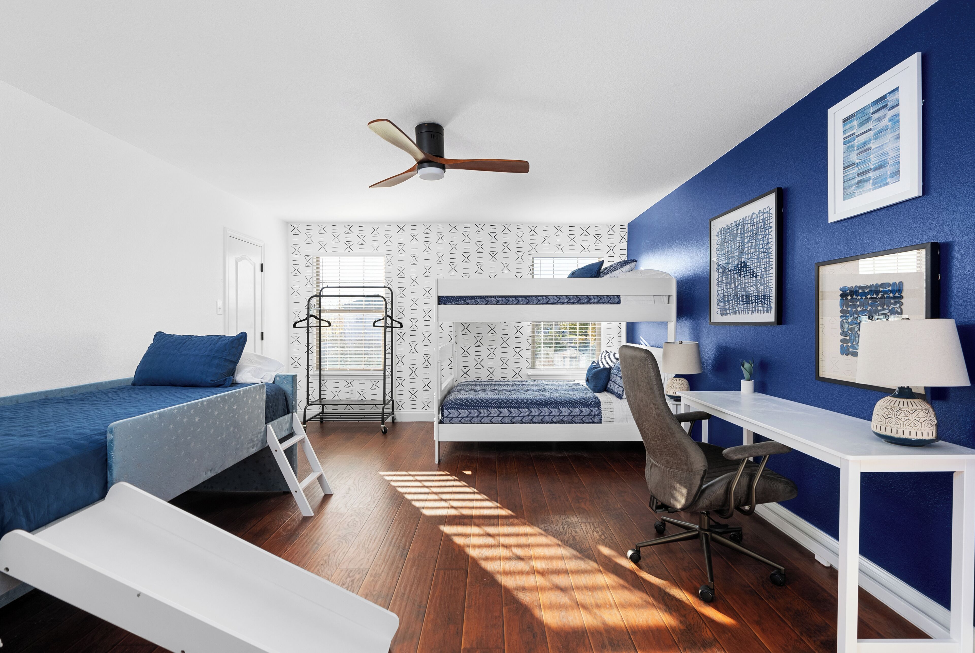 A bedroom with a bunk bed, desk, chair, and a ceiling fan.