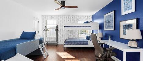 A bedroom with a bunk bed, desk, chair, and a ceiling fan.
