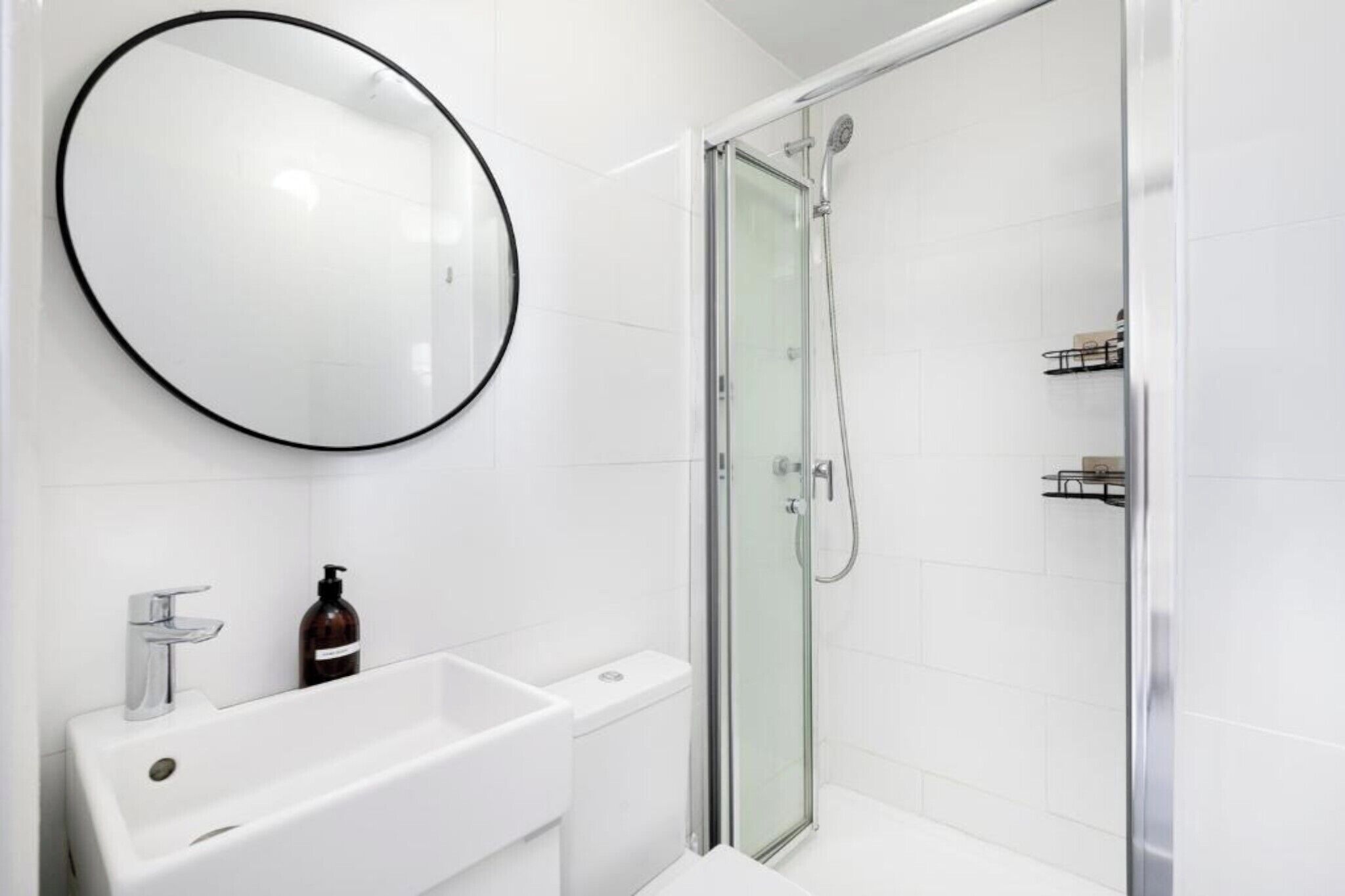 Une salle de bain moderne avec un lavabo blanc, un miroir rond et une douche à parois de verre.