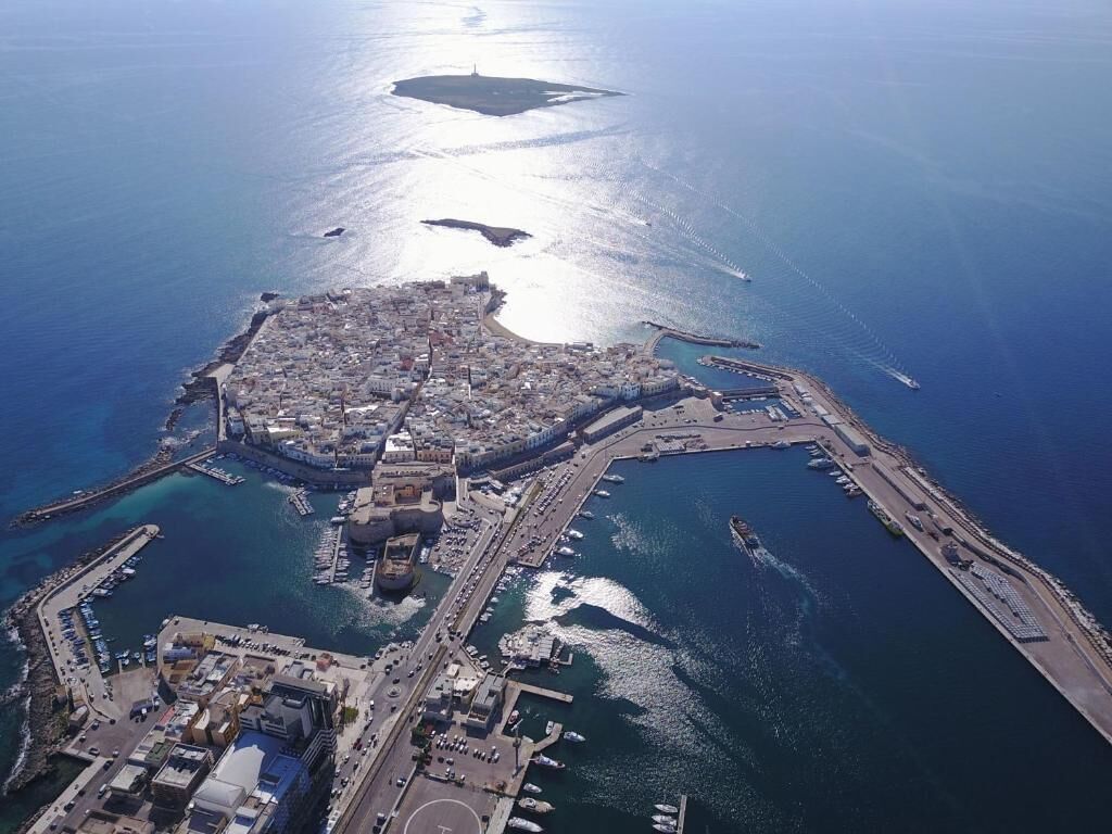 An aerial view of a coastal city with a central peninsula, harbor, and surrounding water.