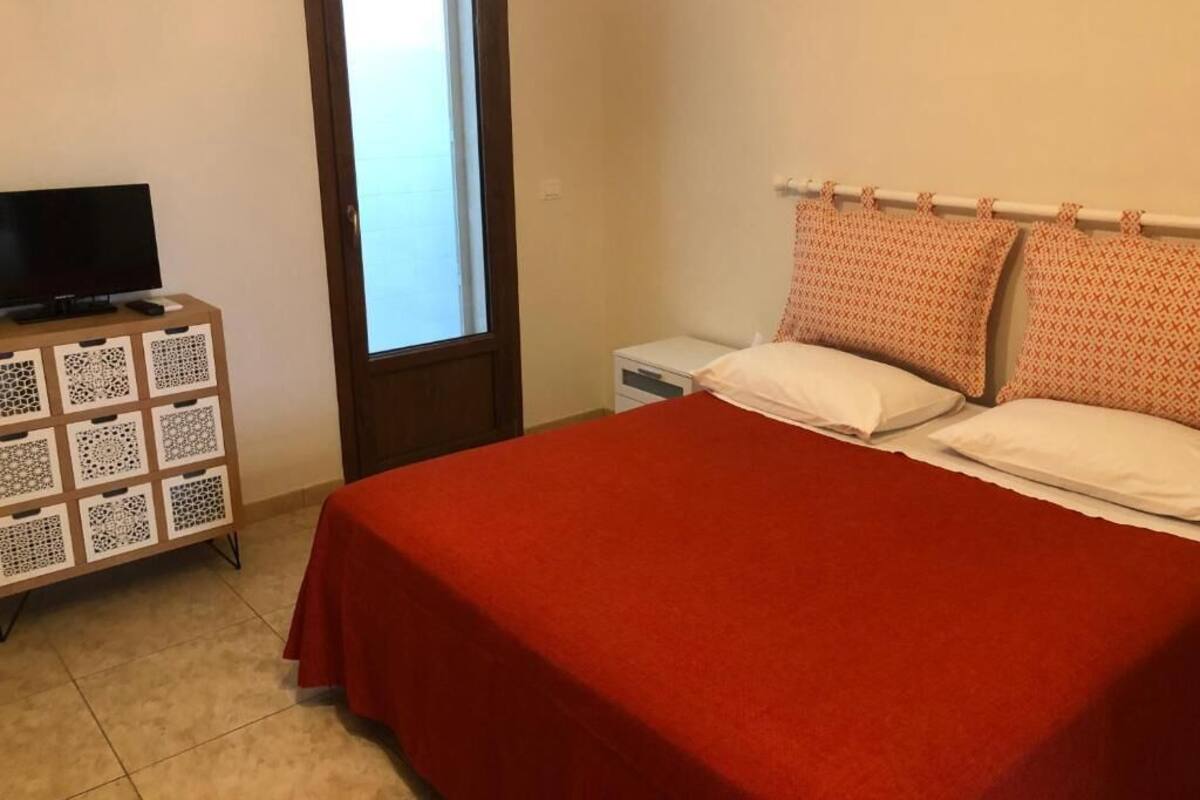 Un dormitori amb un llit, una televisió sobre un moble, una finestra i una porta.