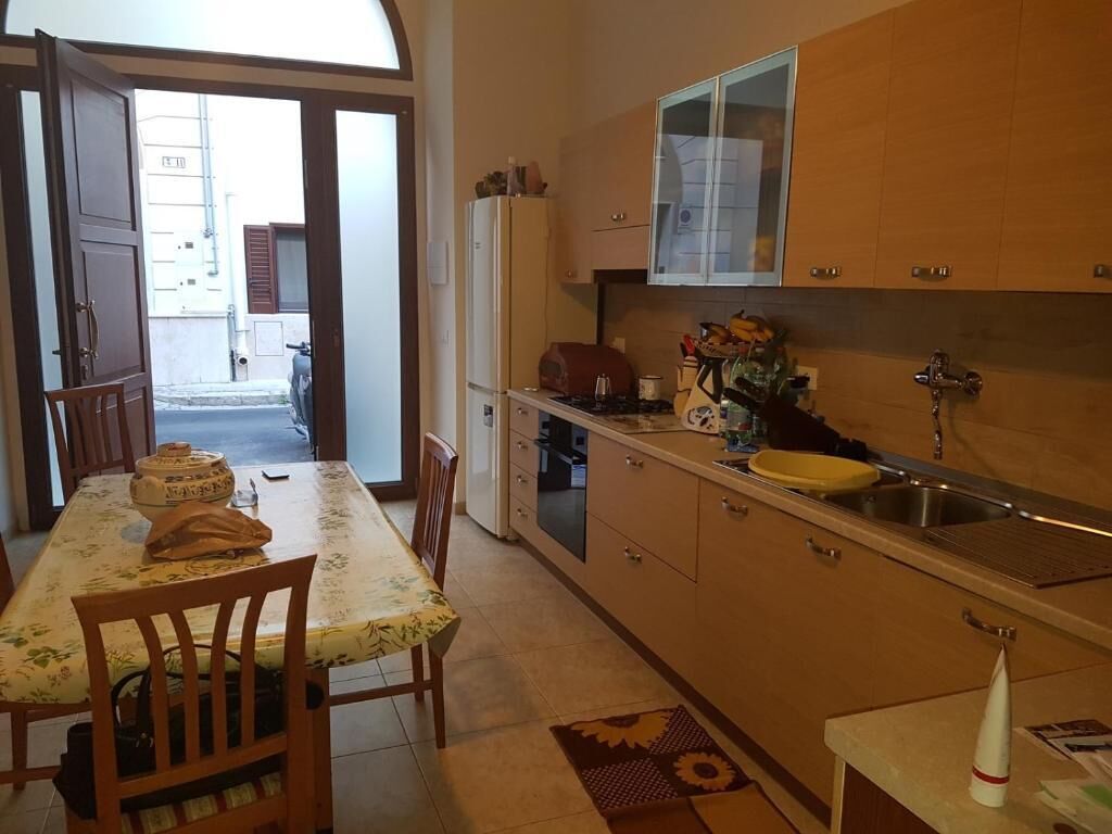 Una cocina con armarios de madera, una mesa de comedor con sillas y vistas a través de una puerta abierta.