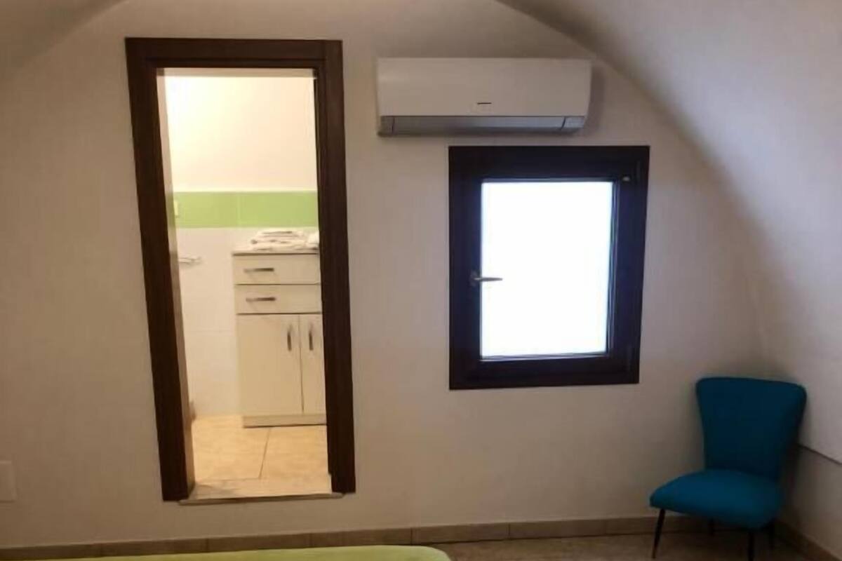Habitació amb un llit, una finestra, una cadira i aire condicionat.