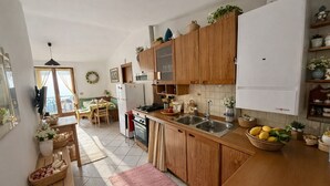 Een kleine keuken met houten kastjes, een inbouwoven, een spoelbak en een eethoek met een tafel en stoelen.