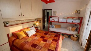 Een slaapkamer met een groot bed, een stapelbed, een bedlampje en een rode paraplu die aan het plafond hangt.