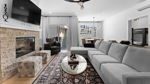 Un salon moderne avec une cheminée, un grand téléviseur à écran plat, un canapé gris et un ventilateur de plafond.