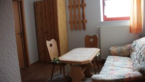 A room with a wooden table, chairs, a sofa, a wooden wardrobe, and a window with curtains. - 2nd standard double room (Benny) in a quiet location in Görlitz (Görlitz)