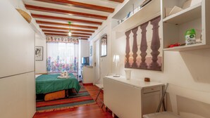 A narrow hotel room with a bed, a desk, a chair, a TV, a window with curtains, and a wooden ceiling. - La Galleria - Piazza di Spagna (Rome)