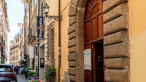 A cobblestone street with a building featuring a large stone archway and a wooden door. - La Galleria - Piazza di Spagna (Rome)