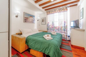 A bedroom with a bed, pillows, a green blanket, a window with a floral curtain, and a television on a stand. - La Galleria - Piazza di Spagna (Rome)