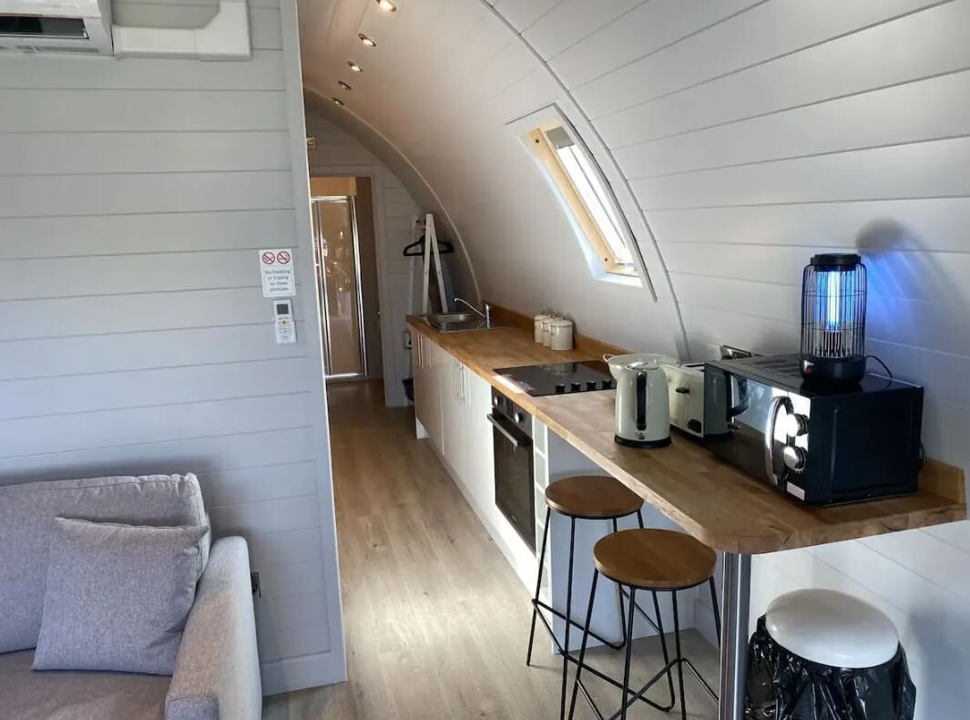Une cuisine compacte dotée d’un plan de travail en bois, de deux tabourets, d’une bouilloire, d’un grille-pain et d’un mixeur.
