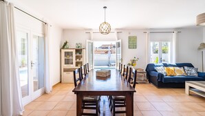 Uma sala de estar espaçosa com uma mesa de jantar, cadeiras, um sofá e um lustre.