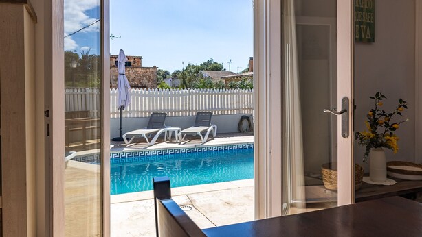 Porta deslizante aberta que dá para área da piscina com espreguiçadeiras e vista livre do bairro ao redor.