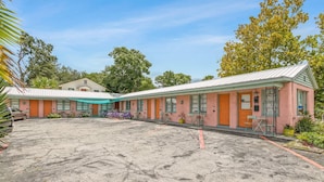 Une rangée de chambres de motel roses, avec un parking devant.