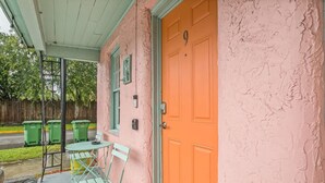 A pink building with a closed orange door, a small table with chairs, and two green trash bins outside. - Travel Back to the 50s- Renovated Motel Gem (St. Augustine)