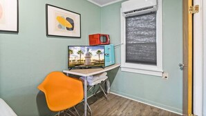 A room with a desk, a chair, a television, a window with blinds, and a door. - Dive Into the 50s- Restored Motel in St Augustine (St. Augustine)