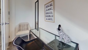 Ein Zimmer mit Glastisch, weißem Stuhl, schwarzem Stuhl, einem gerahmten Motivationsspruch und einer dekorativen Hundfigur.