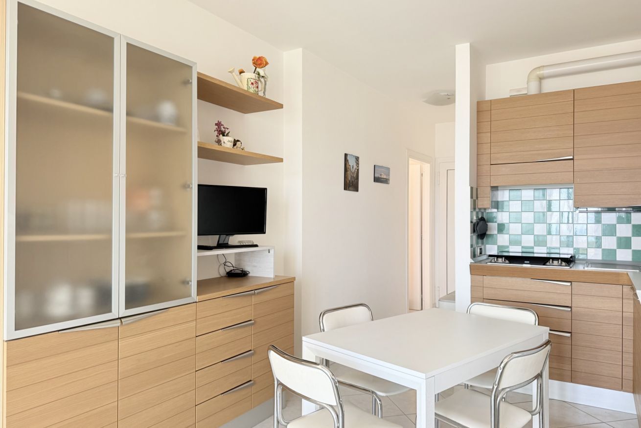 A compact kitchen with a dining area, wooden cabinets, and a television on a stand.