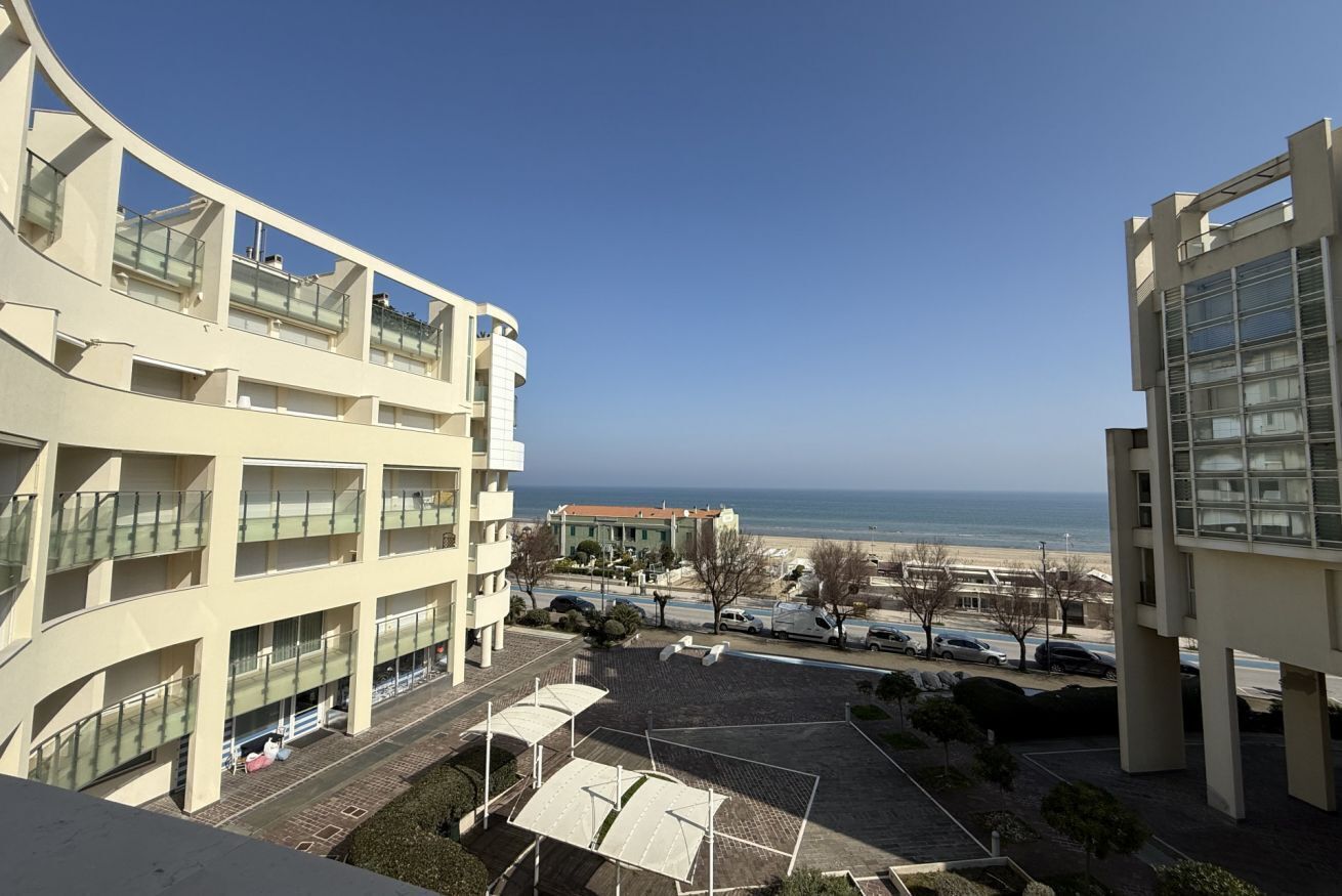 A multi-story building with balconies, a parking area, and a view of the beach.