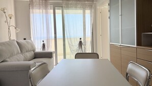 A room with a sofa, a dining table, chairs, a TV, and a view through a window. - SE219 - Senigallia, two-bedroom apartment with a beautiful seafront terrace (Senigallia)