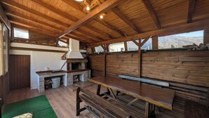Un intérieur rustique en bois, avec une cheminée en pierre, des bancs en bois et une vue sur un paysage montagneux.
