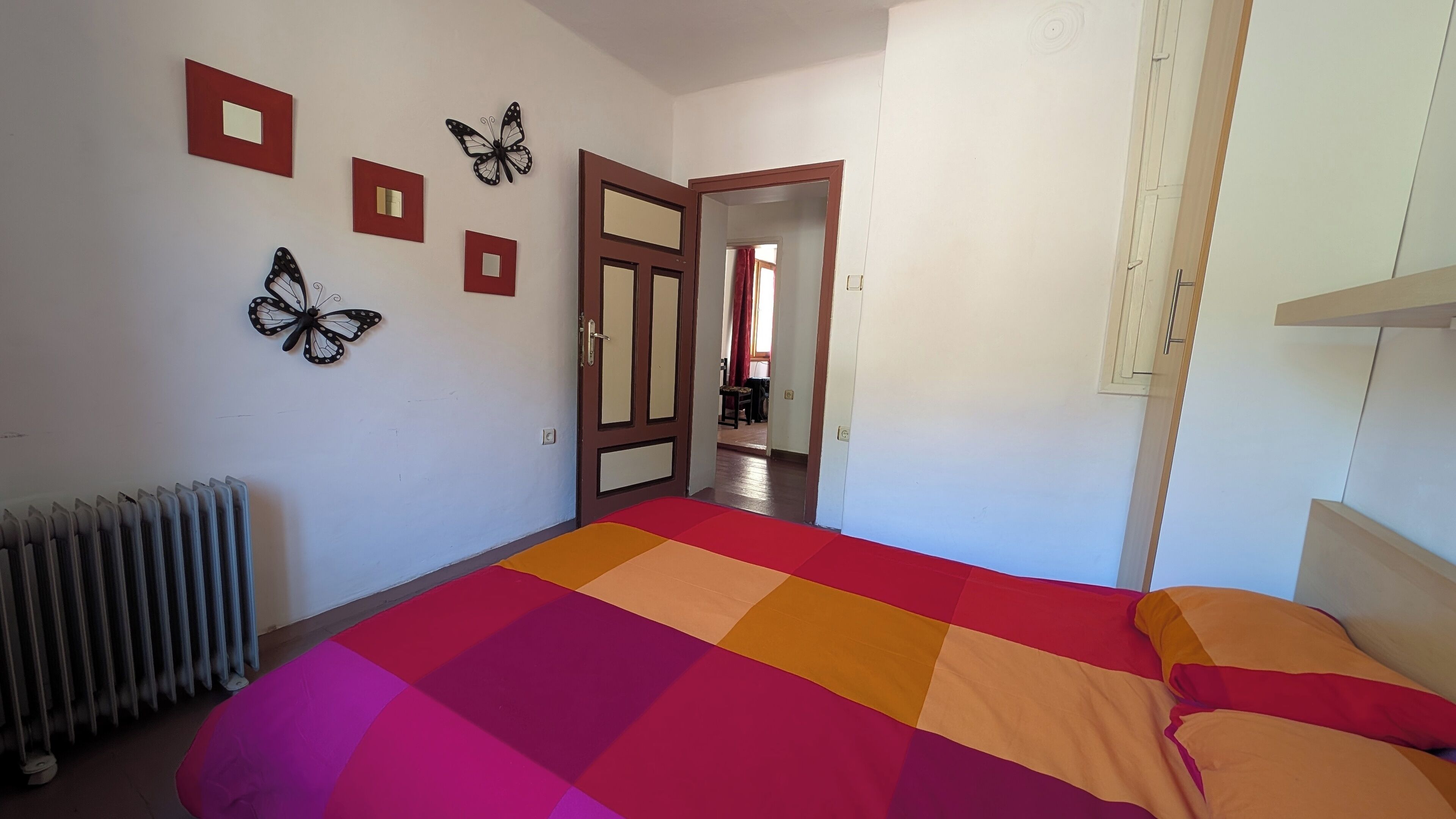 A bedroom with a large bed, a radiator, and butterfly wall art.