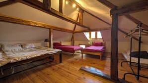 Une chambre à coucher aménagée dans un grenier, avec des poutres en bois, deux lits, un fauteuil suspendu et une fenêtre.