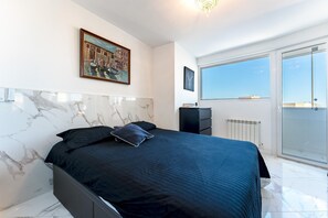 Een moderne slaapkamer met een bed, een marmeren muur, een schilderij, een dressoir en uitzicht door een glazen deur.