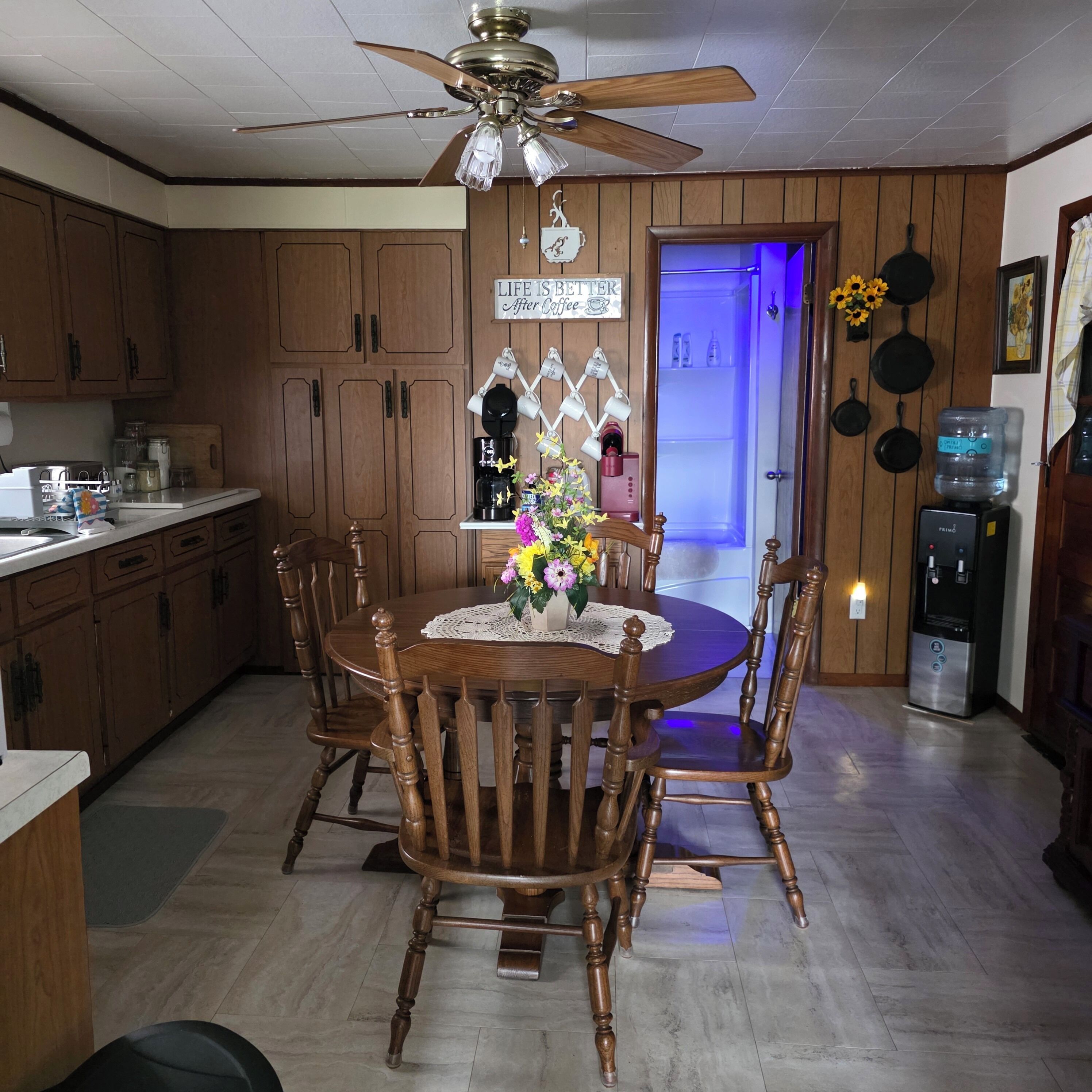 A kitchen with wooden cabinets, a dining table with chairs, a ceiling fan, and a refrigerator.