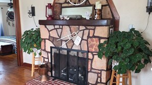 A stone fireplace with a clock above it, flanked by two potted plants, and a brick base.
