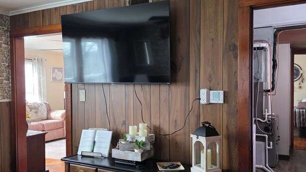 A room with a wooden wall panel, a flat-screen TV mounted above a wooden console, a white lantern, and a remote control on the console.
