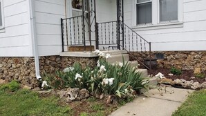 A house with a stone foundation, a front porch with a railing, and a small garden with white flowers.