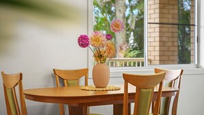Ein Esstisch mit einer Blumenvase, Holzstühlen und einem Fenster mit Blick auf Grünflächen.