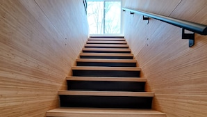A wooden staircase with a metal handrail, leading to a window with a view of trees.