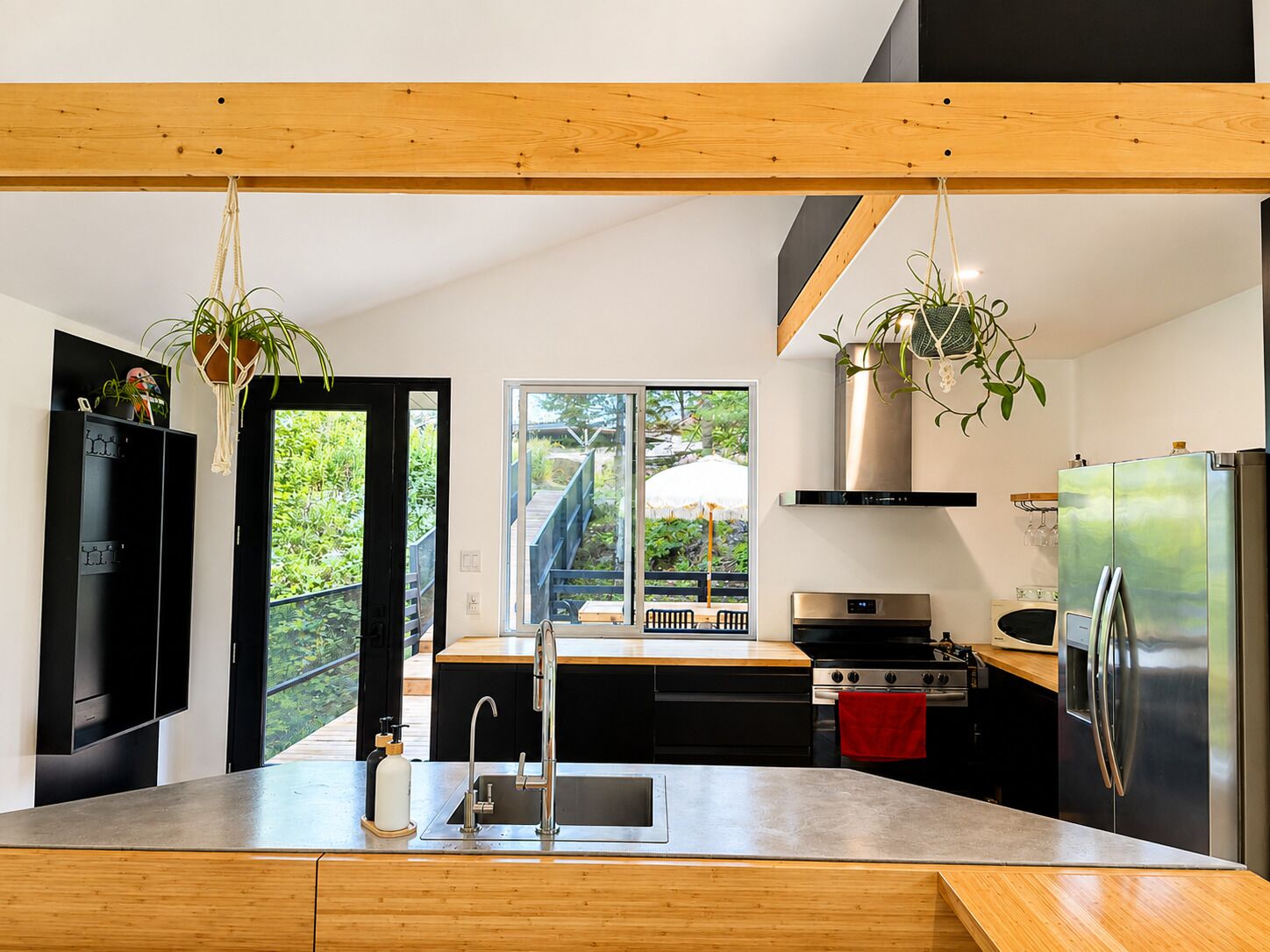 A modern kitchen with a large island, stainless steel appliances, and a view of a wooden deck and outdoor area.