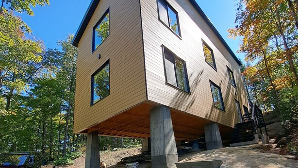 A modern house with a unique floating design, supported by concrete stilts, and accessible by a set of concrete stairs.
