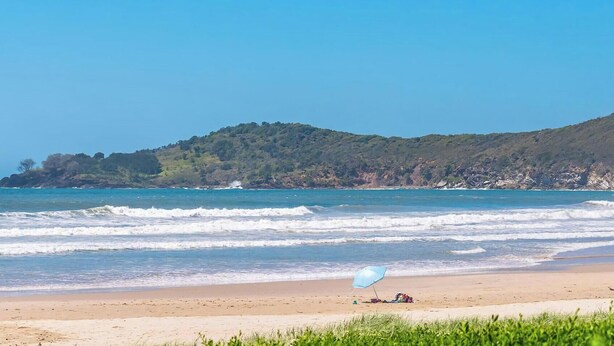 A beach with waves, a clear sky, and a hill with trees. - Comfortable 2BR coastal unit with WiFi, BBQ area, parking & linen included, close to beach (Evans Head)