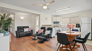 A modern living room with a dining area, a kitchen, and a ceiling fan. - Comfortable 2BR coastal unit with WiFi, BBQ area, parking & linen included, close to beach (Evans Head)