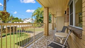 A balcony with a view of a lawn and neighboring houses, a small table, and a chair. - Comfortable 2BR coastal unit with WiFi, BBQ area, parking & linen included, close to beach (Evans Head)